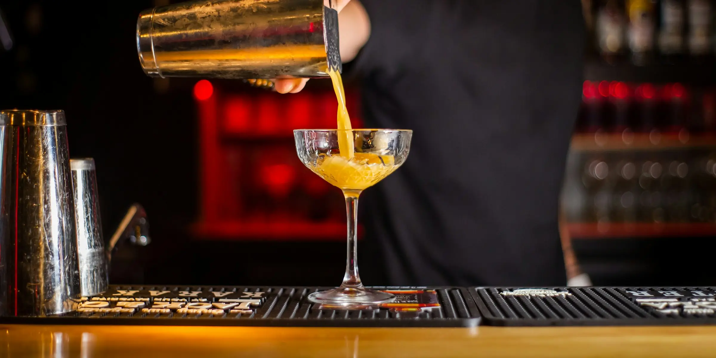 A bartender pours a cocktail from a shaker into a coupe